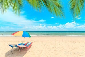 Une plage avec une chaise longue à rayures et un parasol coloré.