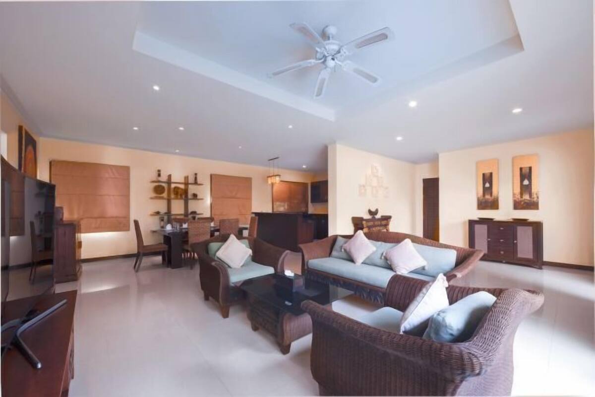 A spacious living area with a ceiling fan, a sofa set, a dining table, and a TV.
