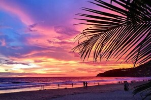 Une scène de plage au coucher du soleil, avec des palmiers et des personnes sur le rivage.