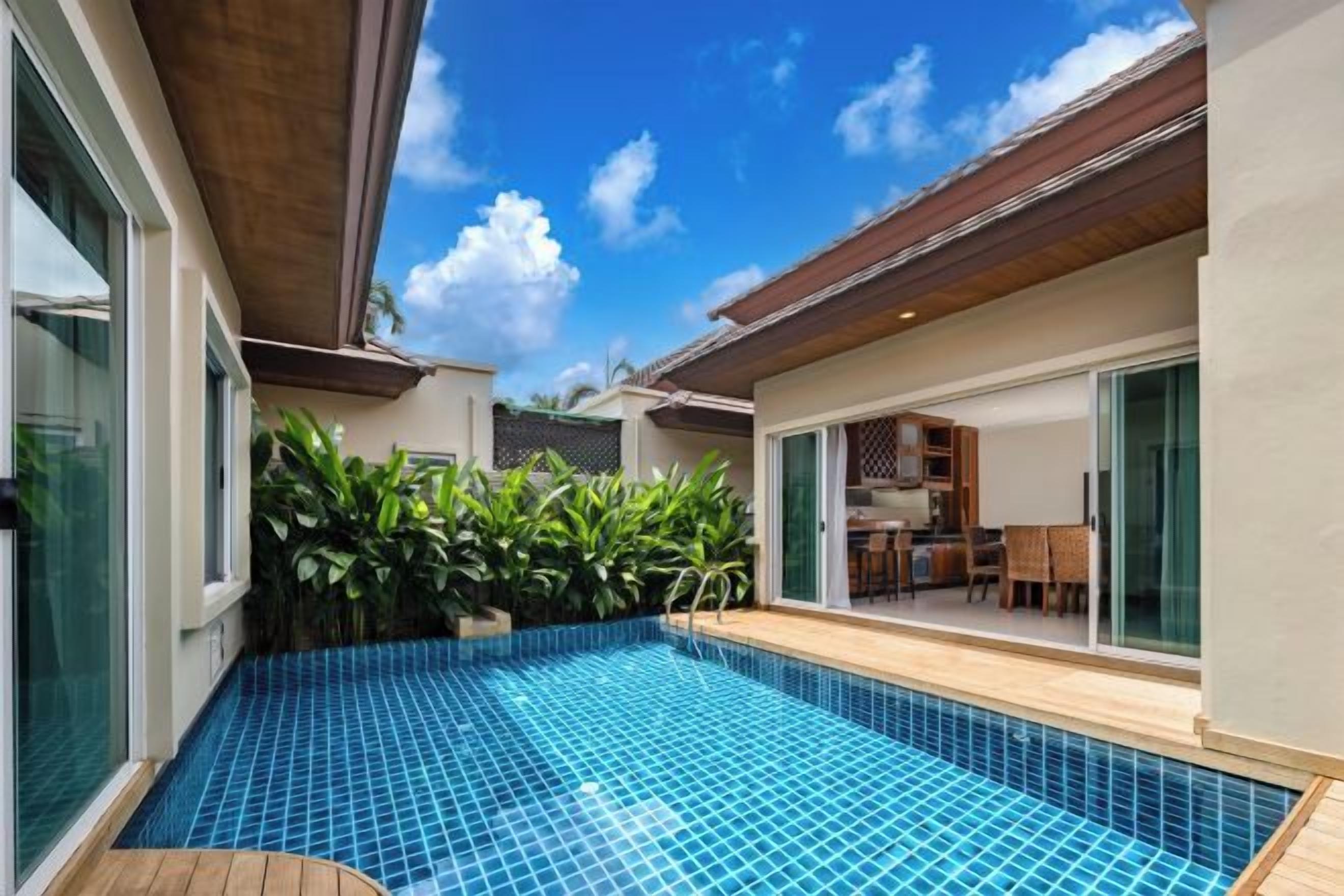 A swimming pool with a tiled floor, surrounded by plants and a wooden deck.