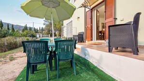 Une terrasse extérieure avec une table et des chaises, un parasol vert et un fauteuil en osier.