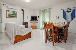 A room with a bed, a TV, a dining table with chairs, and a kitchen area.