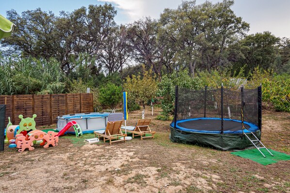 A backyard with a trampoline, pool, and play equipment.