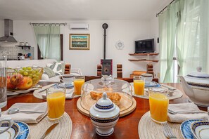 A breakfast setting with a table set for two, including plates, glasses, a teapot, and a fruit basket.