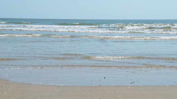 Una spiaggia con onde, cielo sereno e litorale sabbioso.