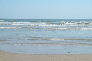 Een strand met golven, een heldere lucht en een zandstrand.