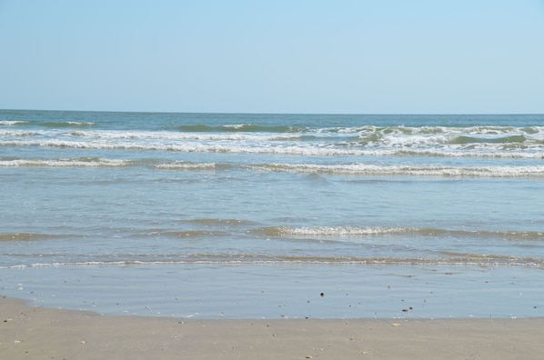 Uma praia com ondas, céu claro e areal arenoso.