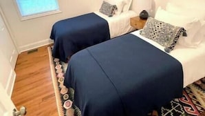 Et soveværelse med to senge, ventilator, et vindue og et mønstret tæppe.