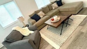 En stue med en beige sofa, en grå lænestol, et træsofabord og en loftsvifte.