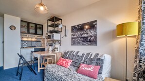 Un espacio habitable compacto con kitchenette, comedor, sofá con tapicería estampada y lámpara de pared.