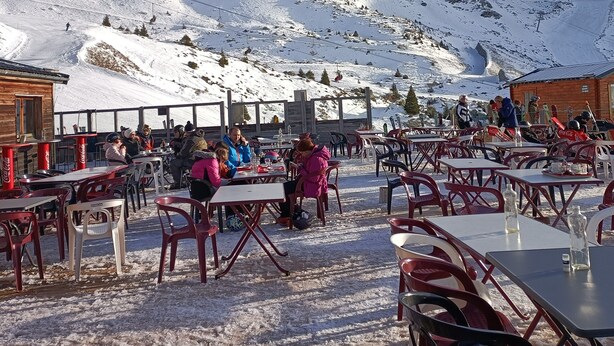 Mesas y sillas al aire libre en un paisaje nevado, con montañas al fondo.
