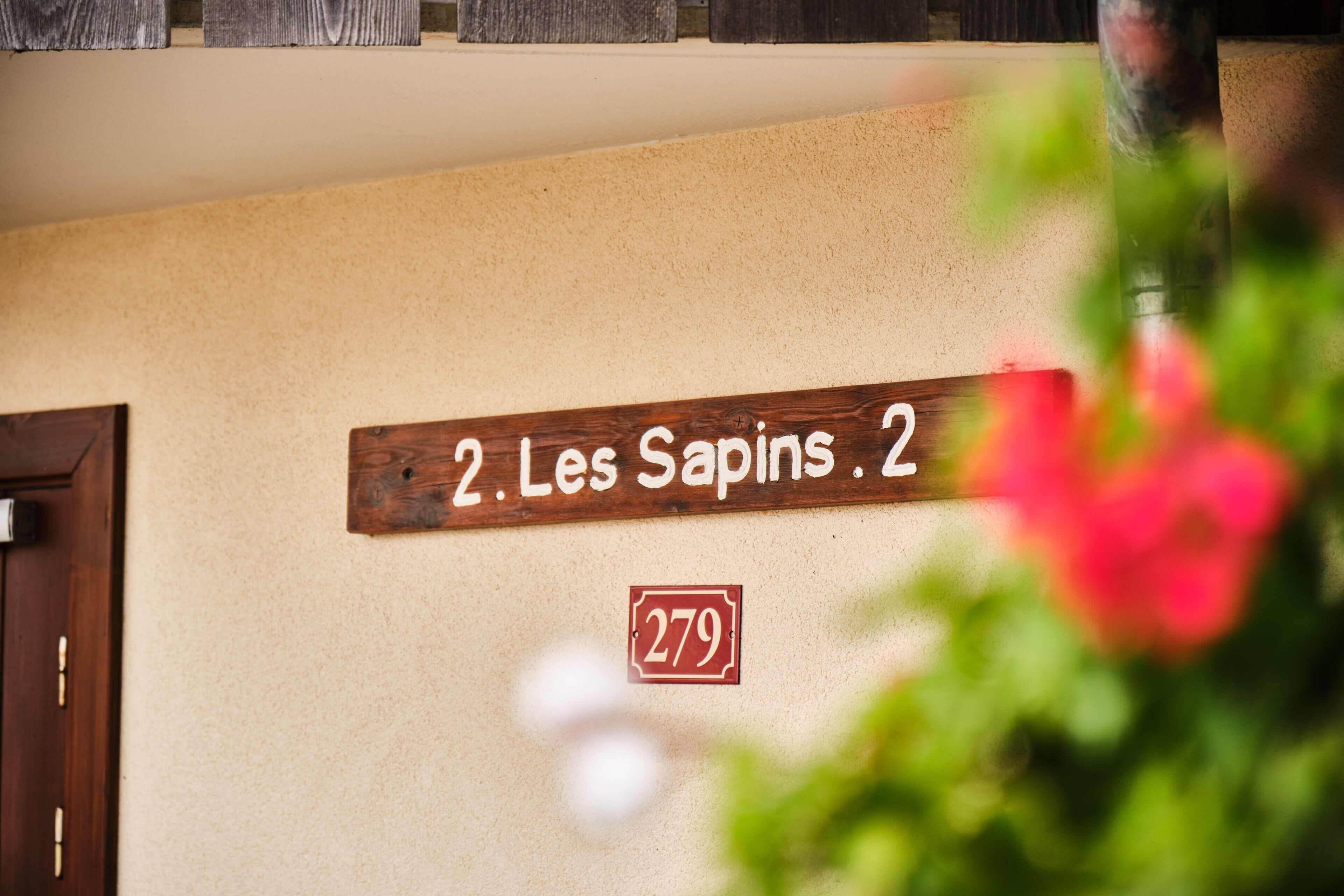 A wooden sign with '2. Les Sapins. 2' and a number '279' on a beige wall.
