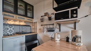 Cocina compacta con refrigerador, microondas, cafetera y salpicadero de azulejos.