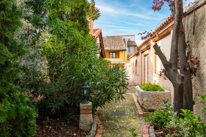 Un étroit sentier de jardin bordé d’une végétation luxuriante et flanqué d’une architecture traditionnelle.