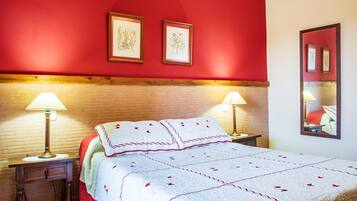 Habitación de hotel con pared roja, cabecera de madera, cama con ropa de cama blanca y detalles rojos, dos lámparas de noche y cuadros en la pared.