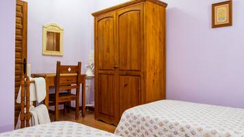 A bedroom with two beds, a wooden wardrobe, a desk with a chair, and a small bedside table.