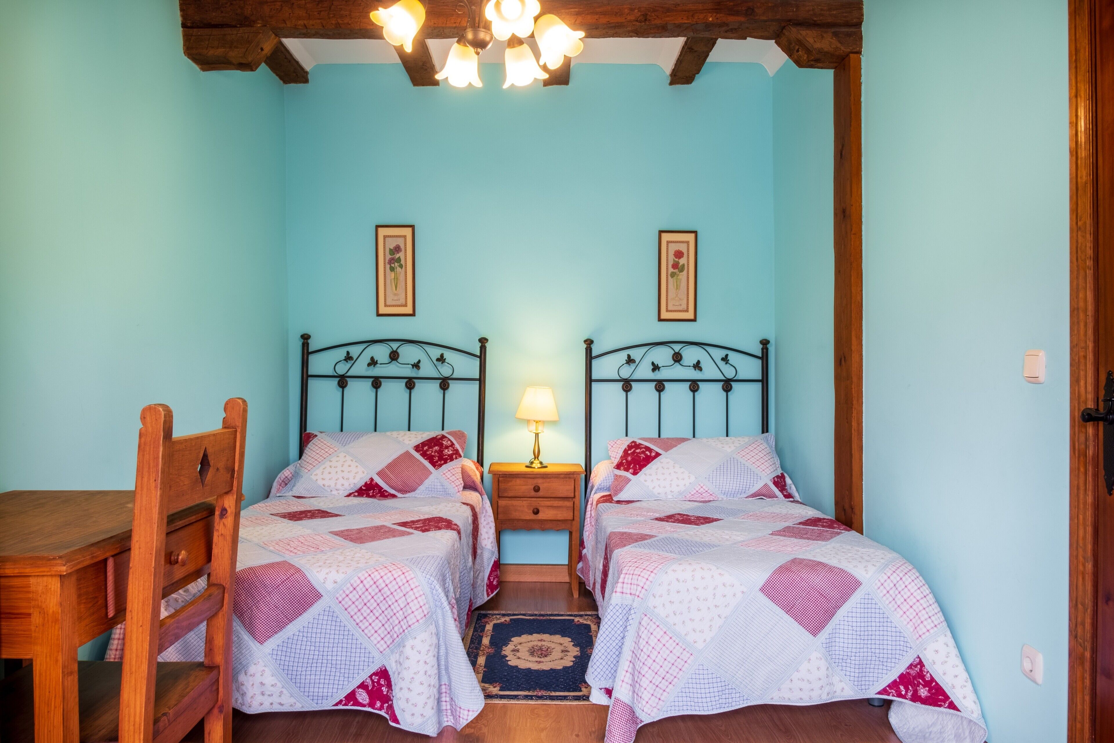 Una habitación con dos camas, un escritorio de madera y una mesita de noche con lámpara.