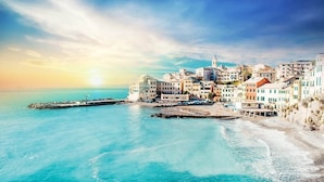 A coastal town with buildings along the waterfront, a pier, and a clear view of the sea.
