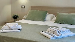 A hotel room with a bed, green pillows, and three framed pictures of the beach on the wall.