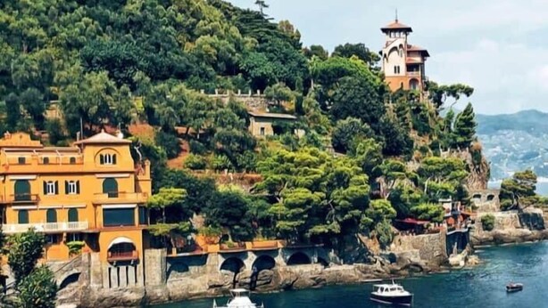 A coastal town with buildings on a hillside, a bridge, and boats on the water.