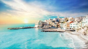 Uma vila costeira com edifícios ao longo da orla marítima, um cais e uma vista ampla do mar.