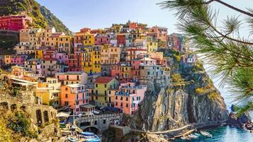 A coastal village with colorful buildings perched on a cliff, a stone bridge, and boats at the harbor.