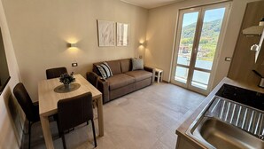 A modern kitchen with a dining area, a sofa, and a large window offering a view of a green landscape. - Apartment N.6, Appartamento N.6 Secondo Piano (San Salvatore)