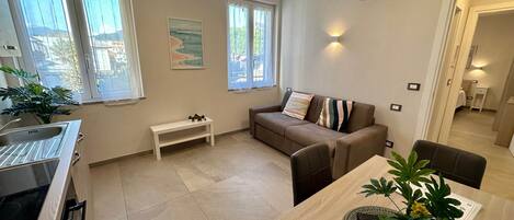 A modern apartment with a kitchen, dining area, and living room. It features a sofa, a dining table, and a bench.
