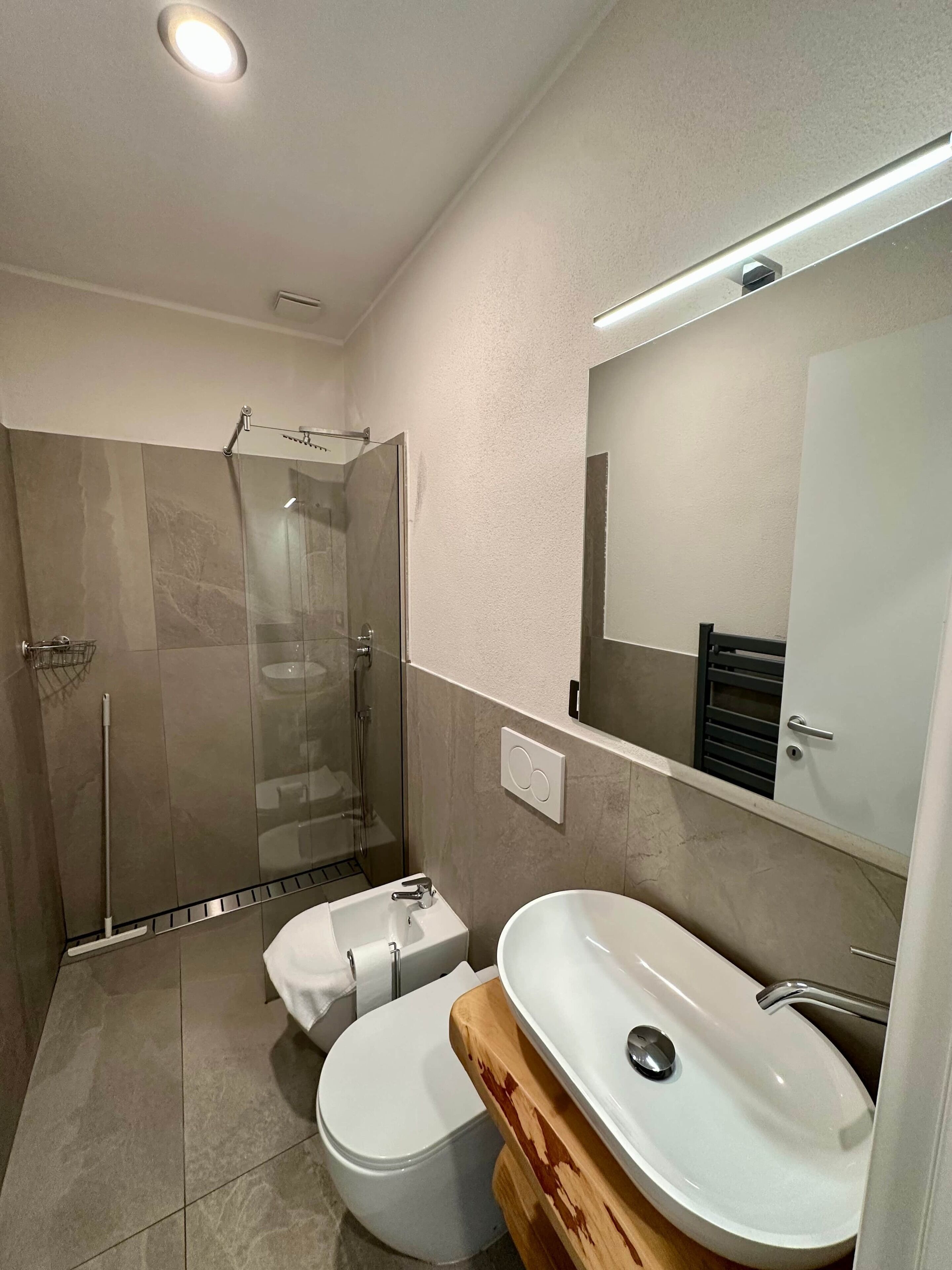 A modern bathroom with a glass-enclosed shower, a white toilet, and a wooden vanity with a sink.