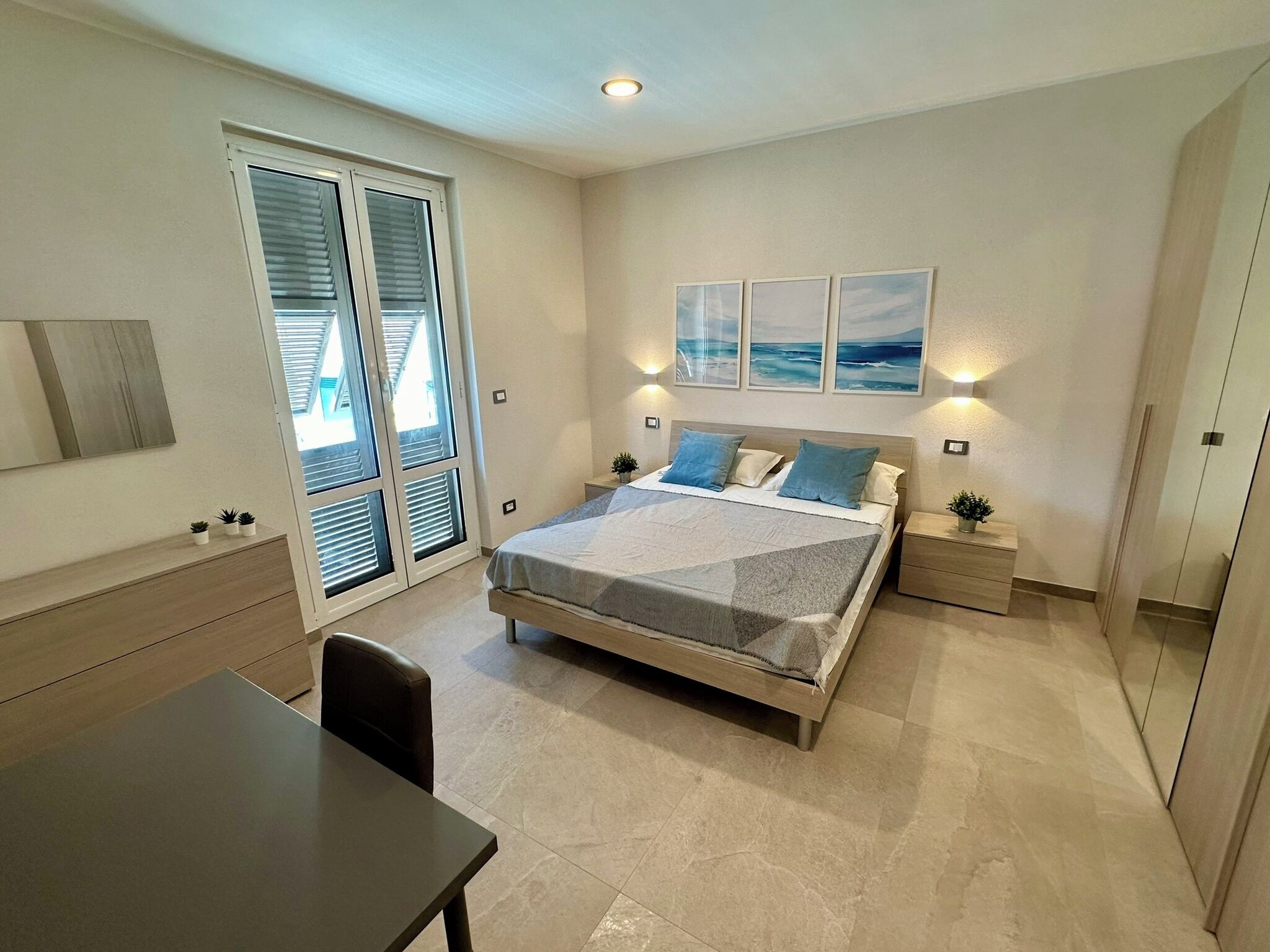 Une chambre à coucher avec un lit, des tables de chevet, un bureau et une chaise. Trois tableaux encadrés sont accrochés au mur.