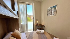 Ein ordentlich bezogenes Bett mit Kissen, einer Decke und einem gefalteten Handtuch. Durch eine Schiebetür ist ein Blick ins Freie möglich.