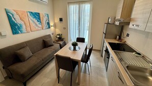 A compact living space with a kitchenette, a dining area with a table and chairs, a sofa, and artwork on the walls.