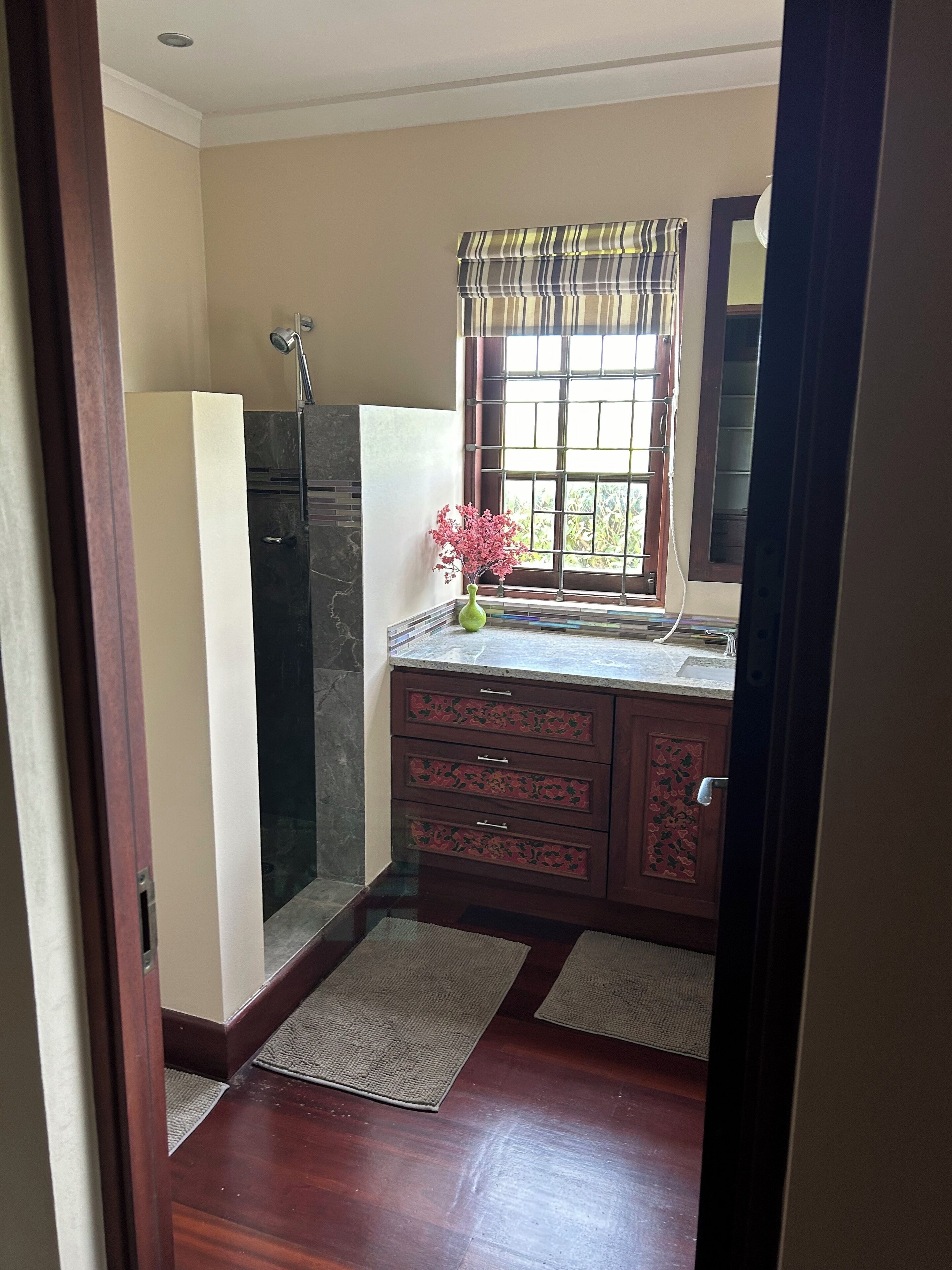 A bathroom with a shower, a sink, and a window with curtains.