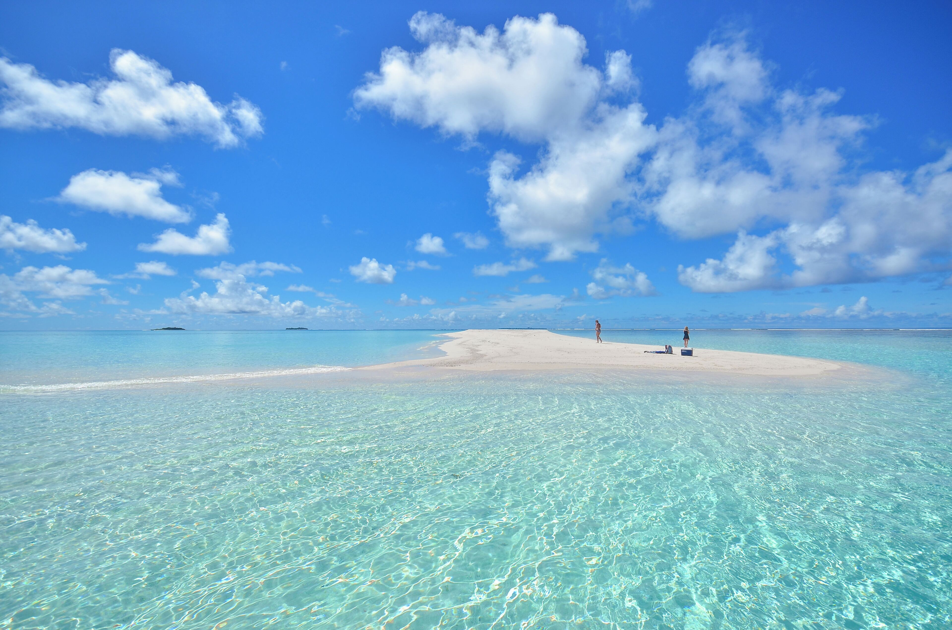 A clear turquoise sea with a sandy beach and a few people.