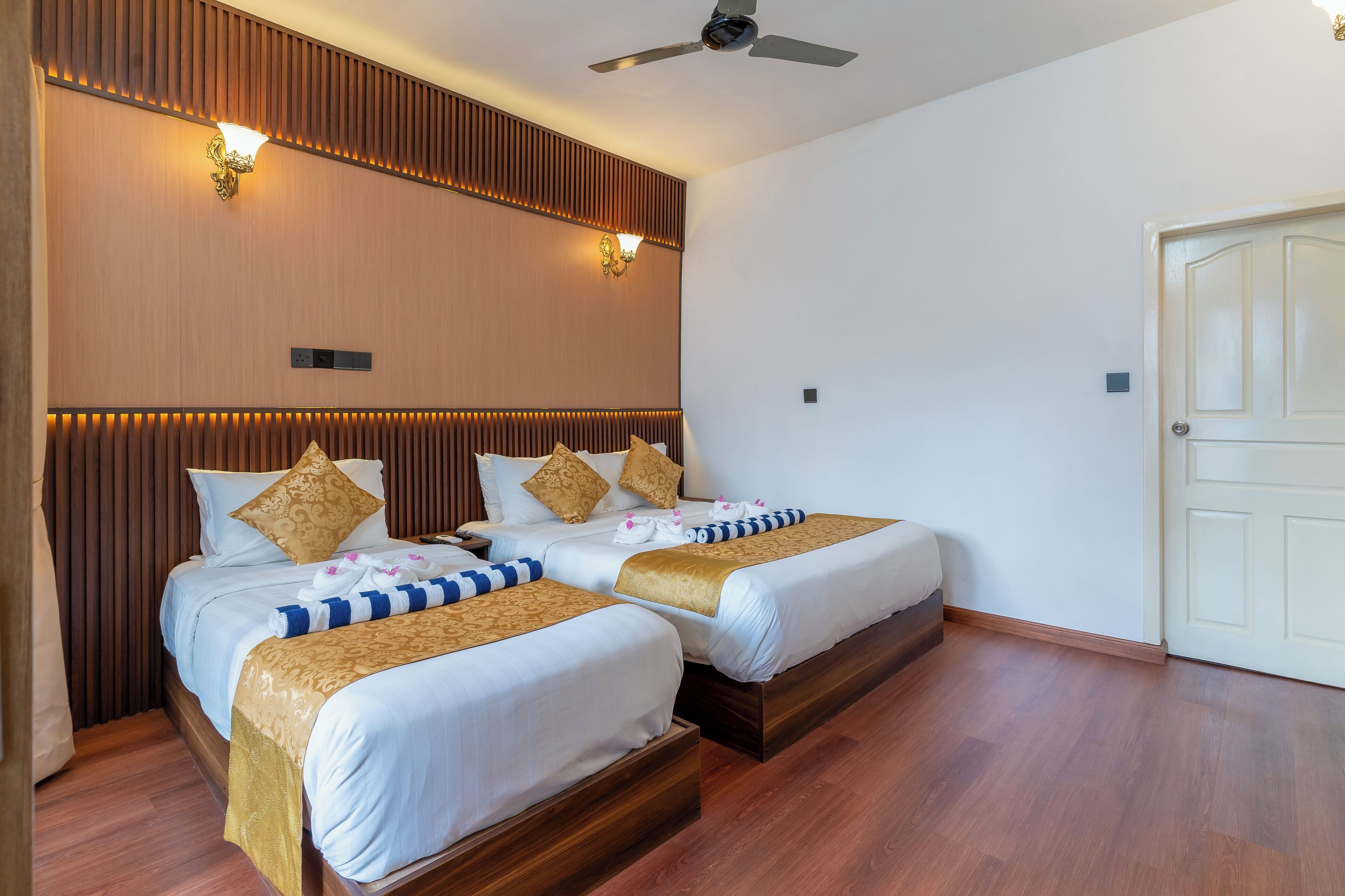 Habitación de hotel con dos camas, paneles de madera en las paredes y un ventilador de techo.