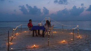 A beach dinner setup with a table and chairs, surrounded by string lights. - Ganduvaru Villa (Ukulhas)