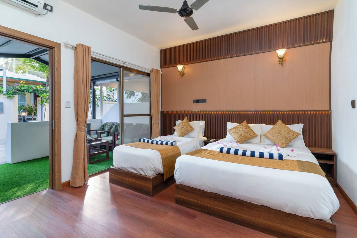 A hotel room with two beds, a ceiling fan, and a sliding glass door leading to an outdoor area.