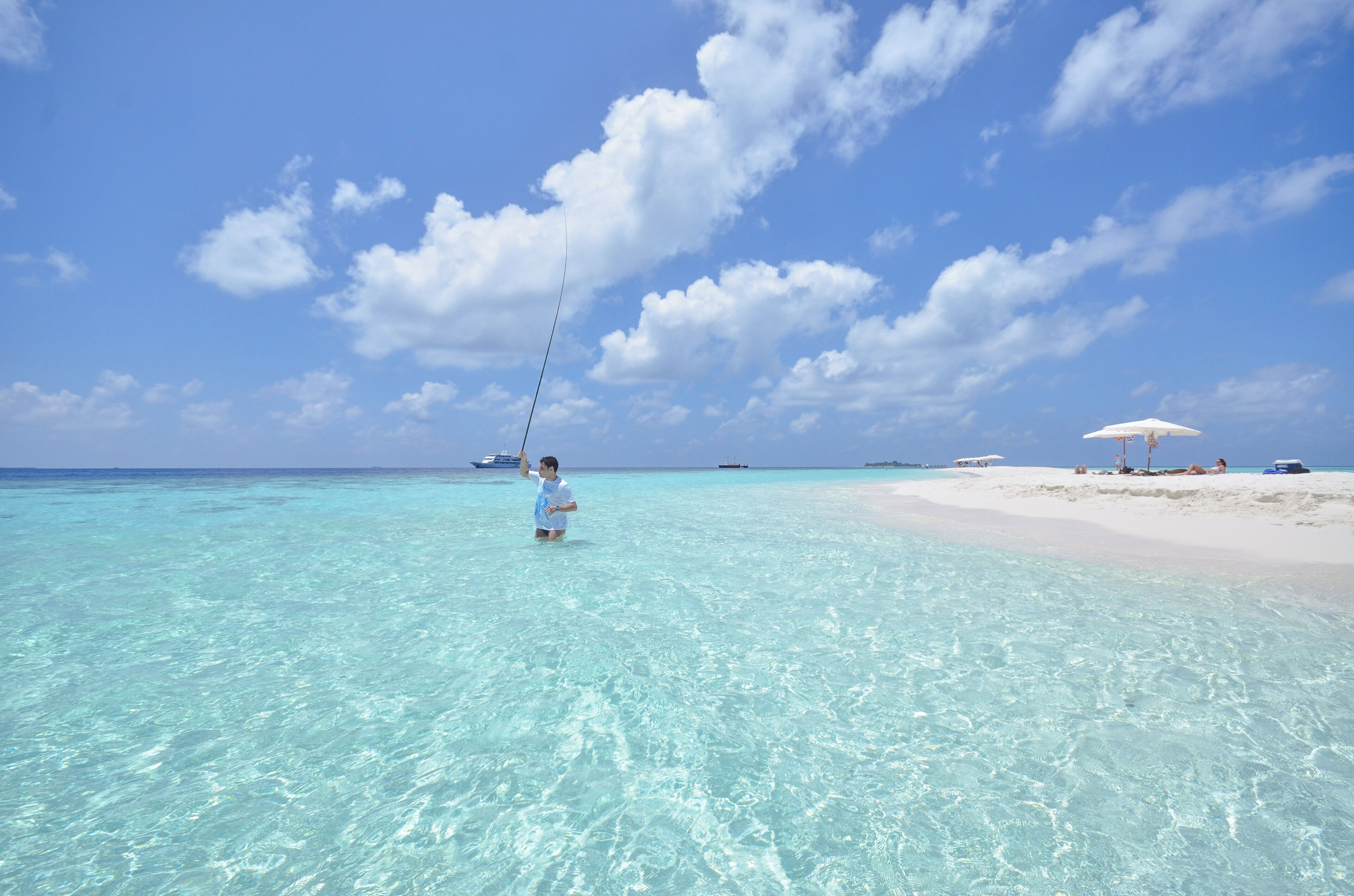 A beach scene with clear turquoise water, a sandy shore, and a few boats in the distance.