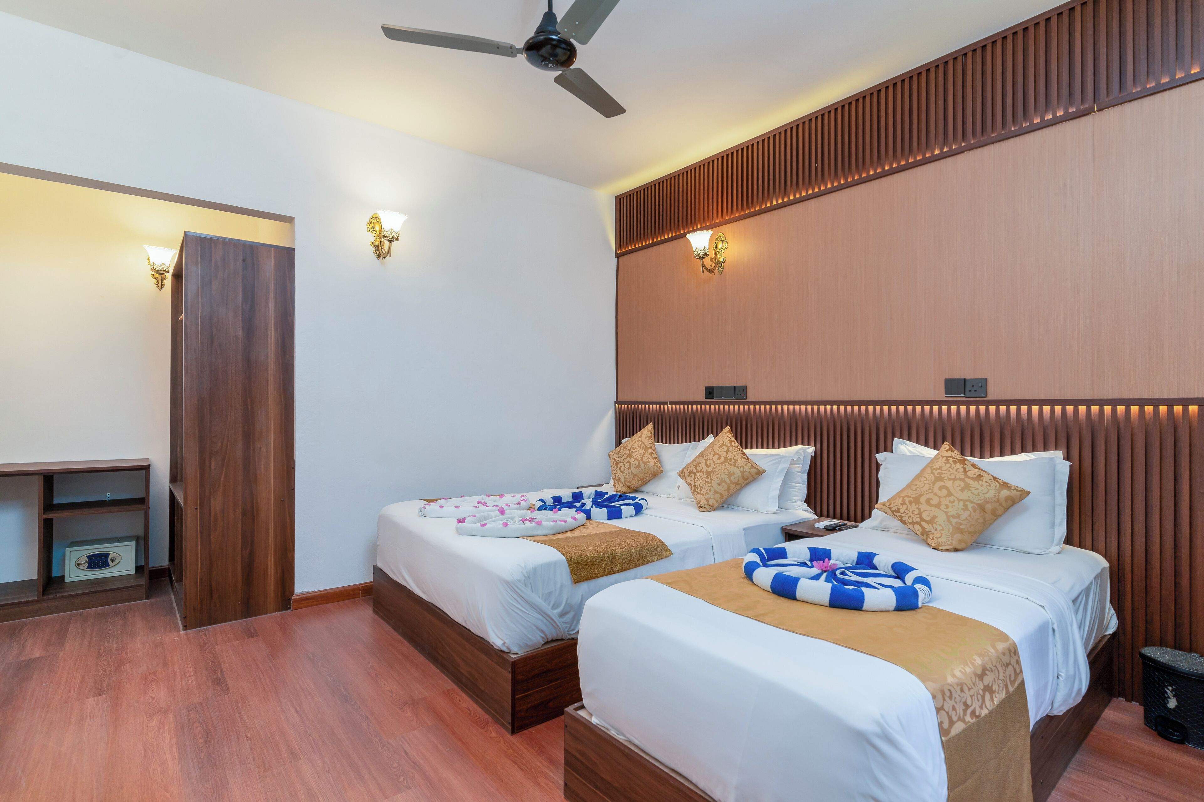A hotel room with two beds, a ceiling fan, wooden paneling, and a small desk with a lamp.
