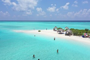 A beach with clear turquoise water, a sandy shore, and thatched-roof structures. - Ganduvaru Villa (Ukulhas)