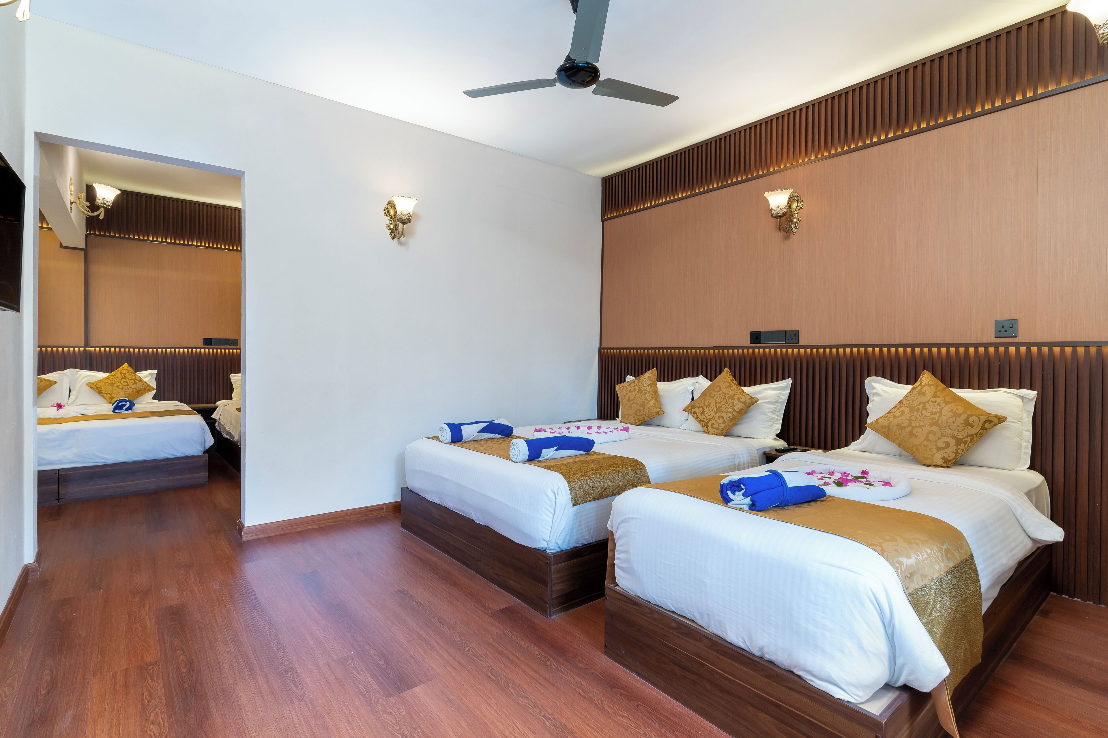 A hotel room with three beds, wooden paneling, and a ceiling fan.
