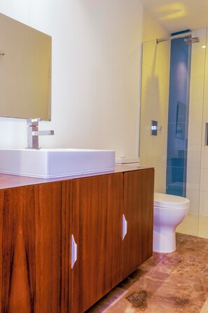 Ein modernes Badezimmer mit einem hölzernen Waschtisch, einem weißen Waschbecken und einer Duschkabine aus Glas.