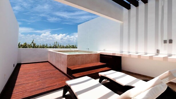 Un área lounge moderna al aire libre con terraza de madera, sillas reclinables blancas y un jacuzzi integrado.