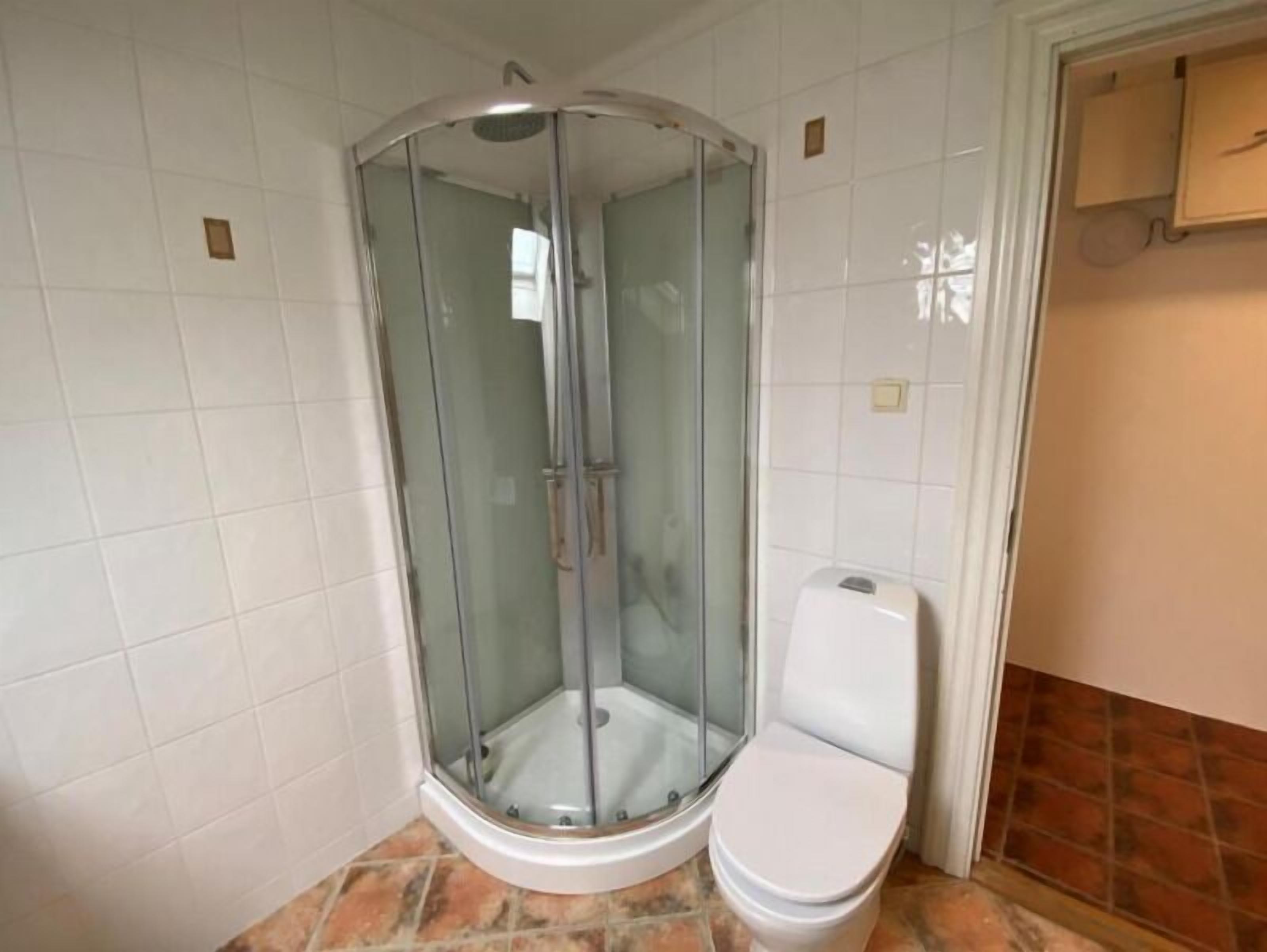 A corner shower enclosure with a glass door, a white toilet, and a tiled floor.
