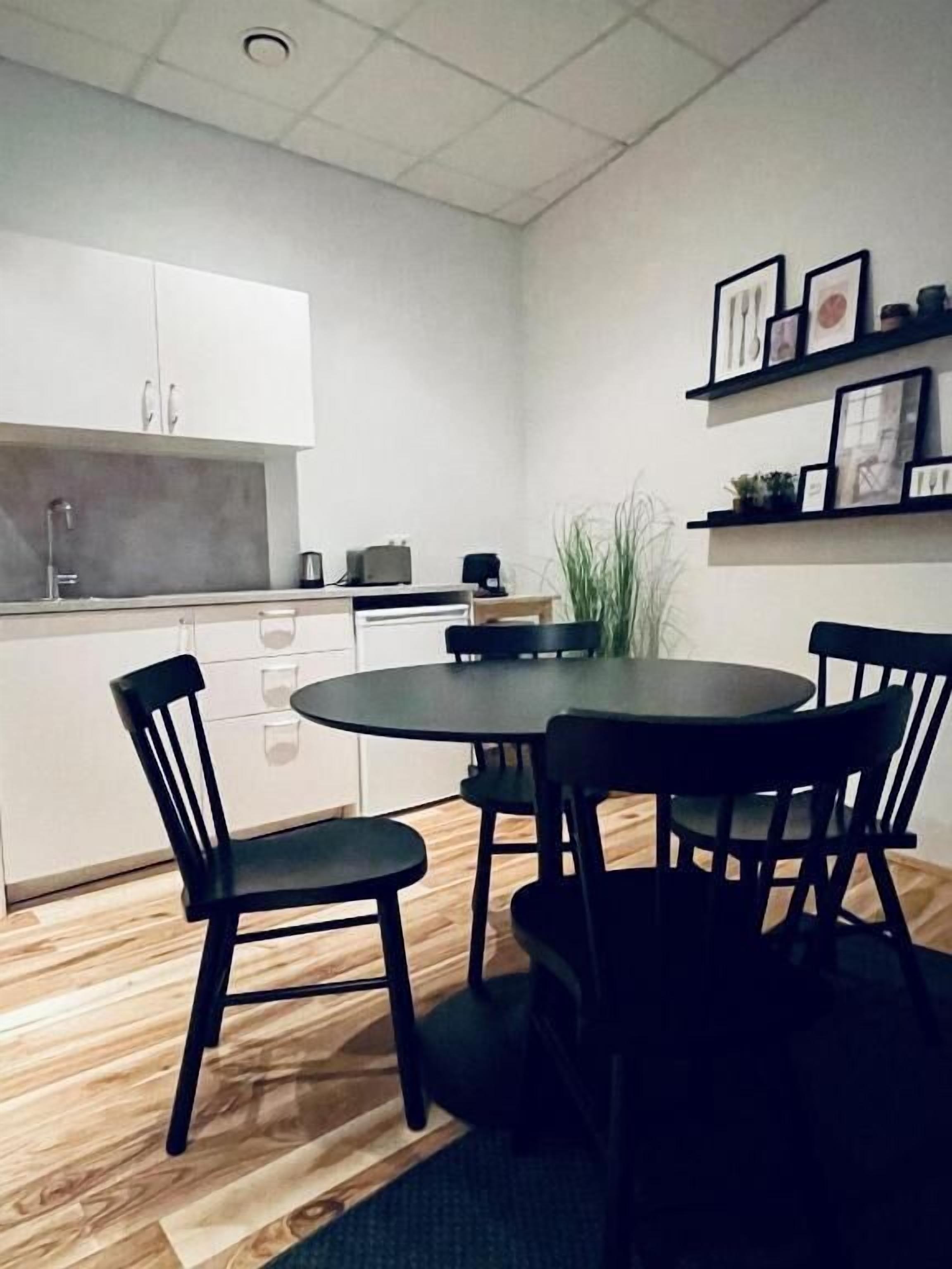 Una cocina compacta con armarios blancos, una mesa redonda de comedor y sillas negras.