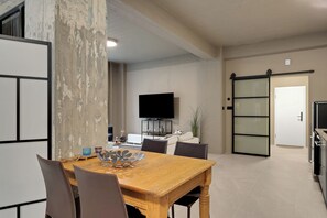 Ein modernes Wohnzimmer mit einem Holzesstisch, Stühlen, einem Flachbildfernseher und einer Glastür, die in eine Küche führt.