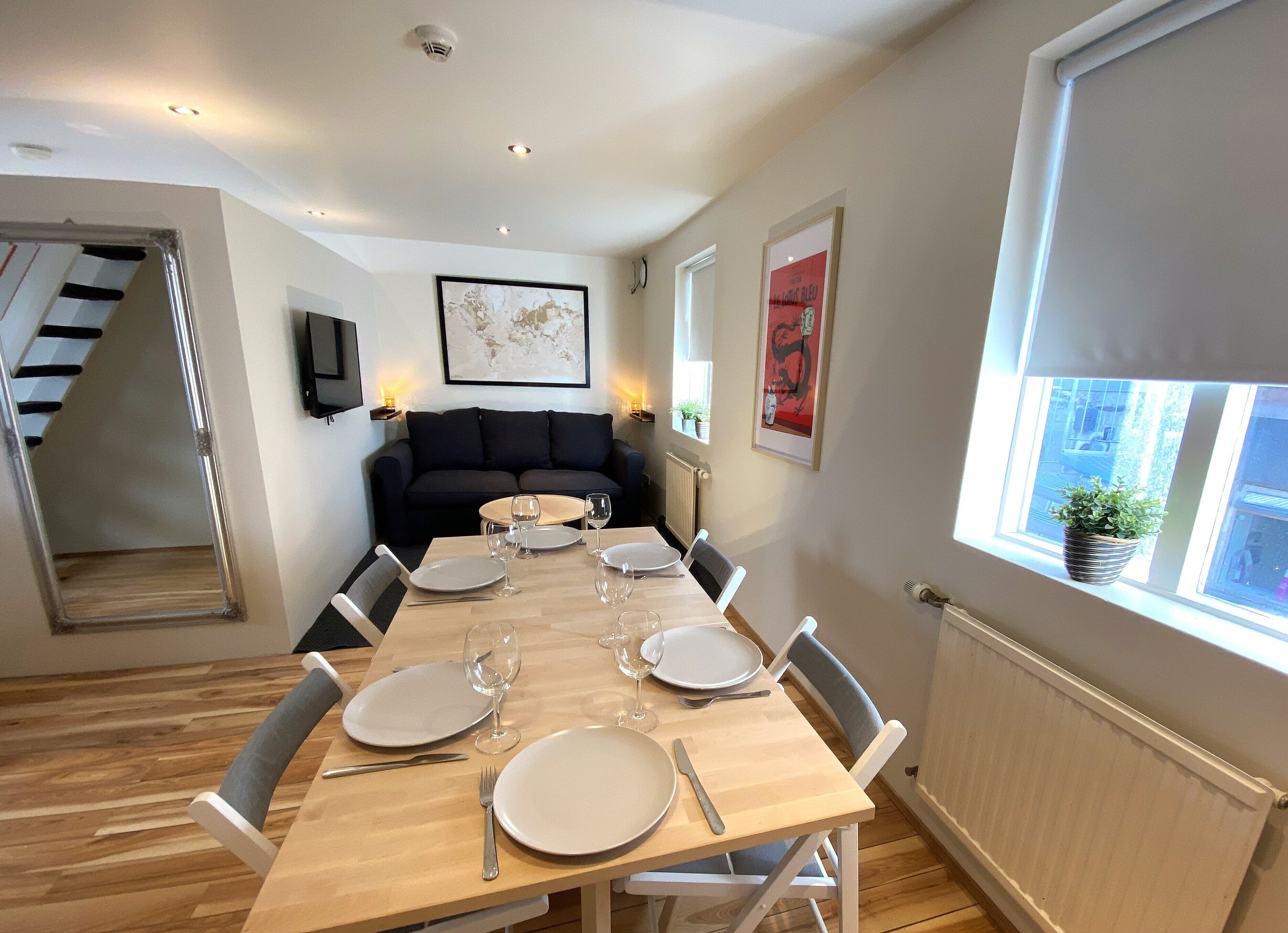 A dining area with a wooden table set for six, flanked by two black sofas.