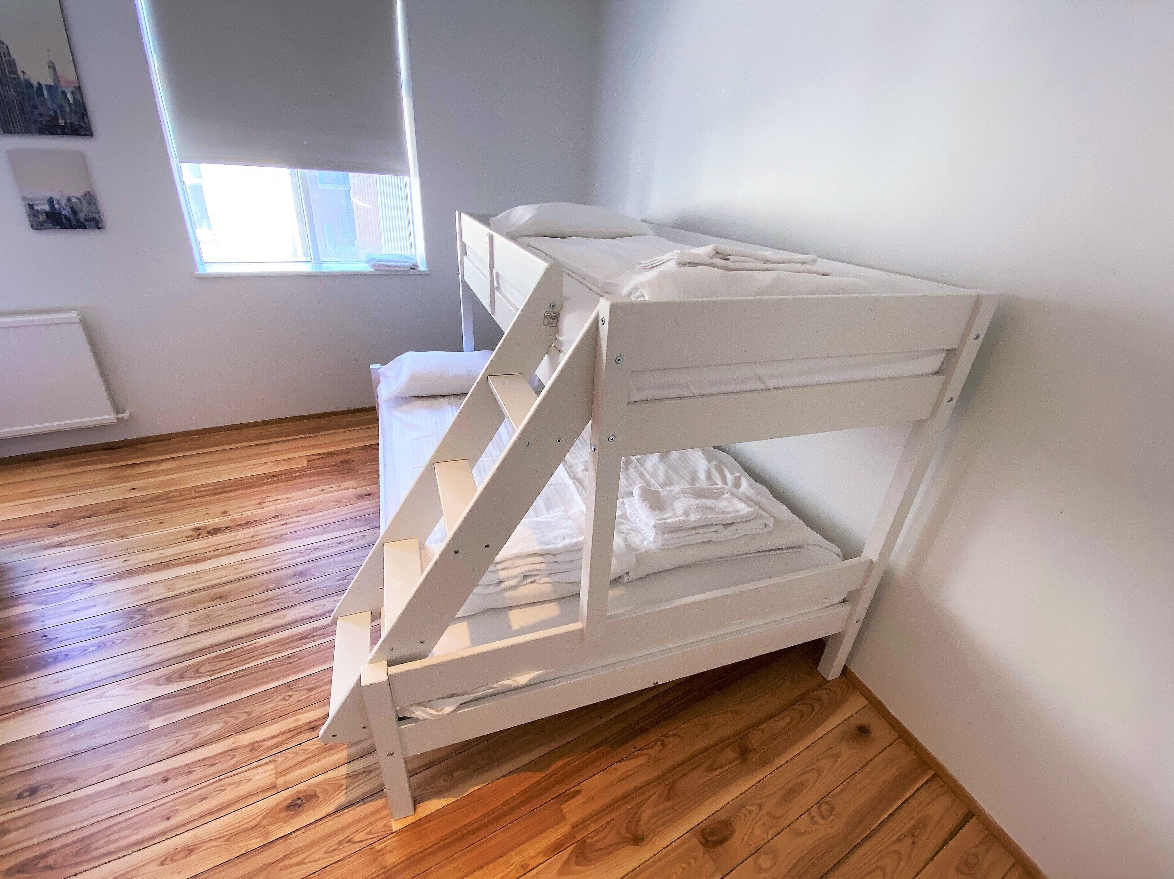A white bunk bed in a room with wooden flooring and a window.