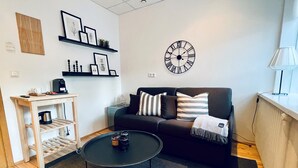 Una sala de estar moderna con un sofá negro, una mesa de centro, un reloj y una estantería con marcos de fotos.