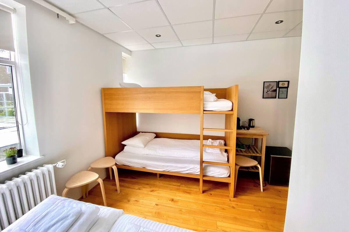 A bunk bed room with a wooden desk and chair, a radiator, and a window.